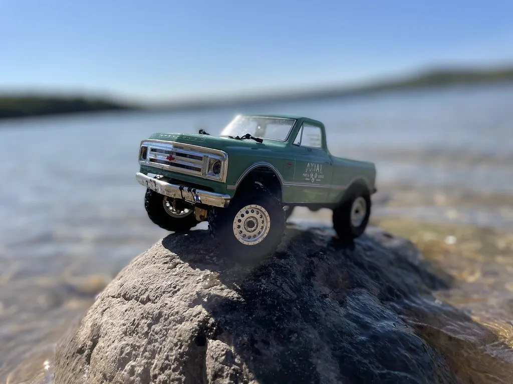 Camioneta crawler RC verde sobre una roca a la orilla de un lago