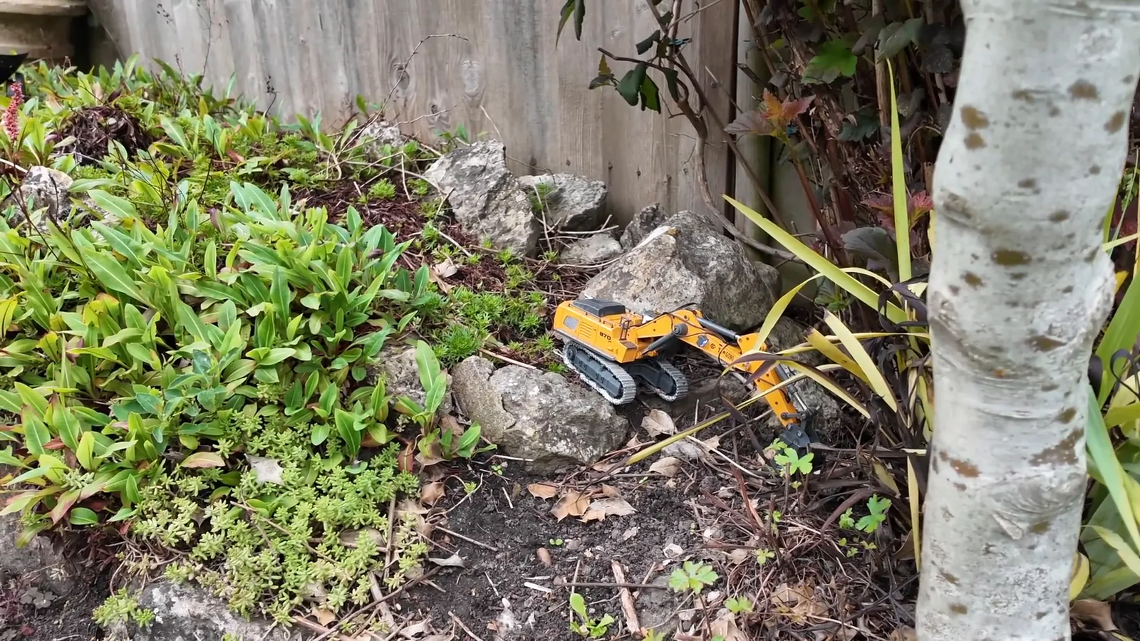 Excavador RC escalando una pendiente con pistas metálicas y funcionando a plena capacidad